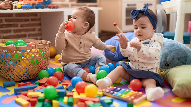 Deux enfants de moins de trois ans jouent avec des balles en plastique dans un lieu qui ressemble à une crèche
